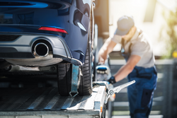 A man in overalls loading a car onto the back of a recovery vehicle