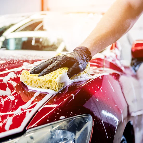 worker cleaning red car with sponge